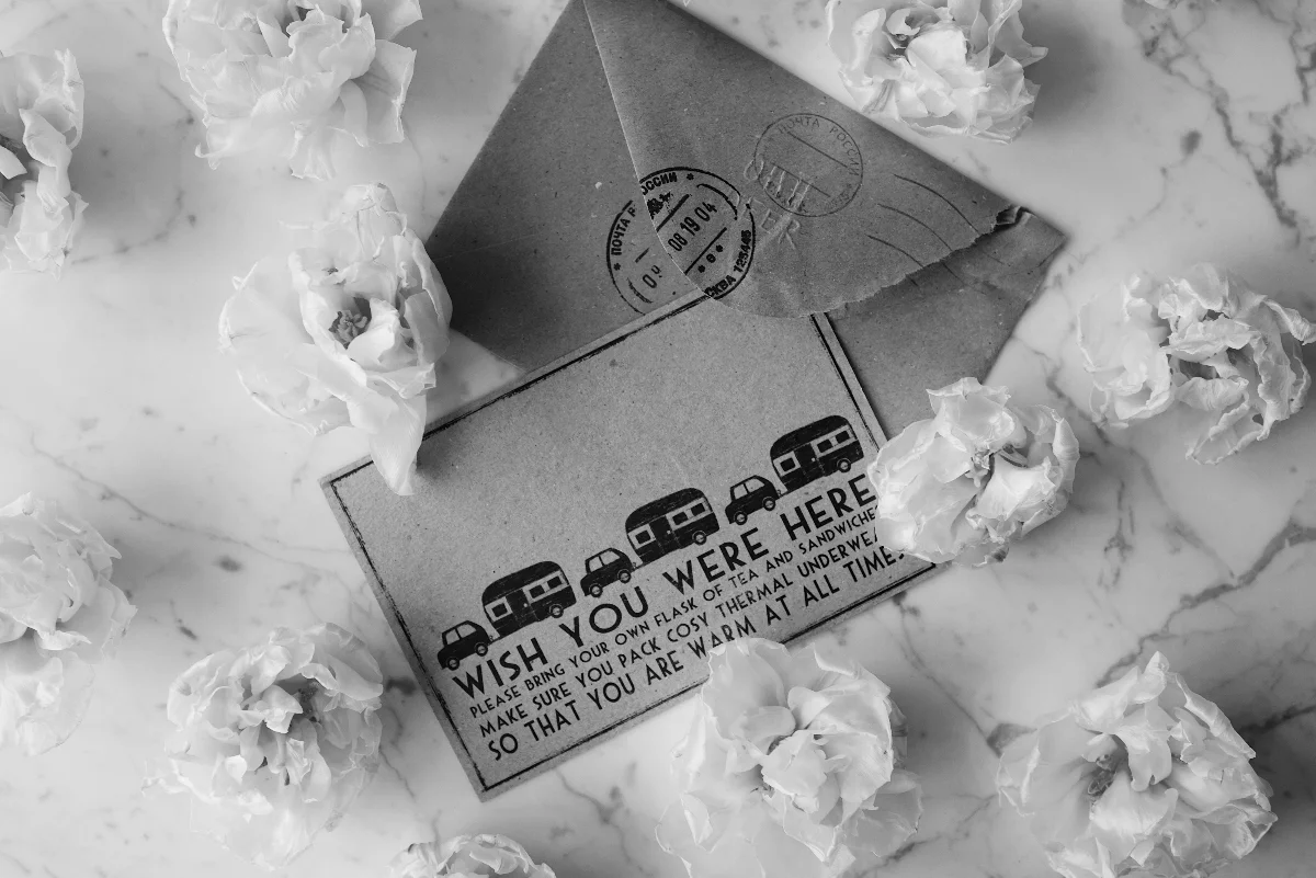A black and white photo of a vintage postcard surrounded by flowers on a marble surface.