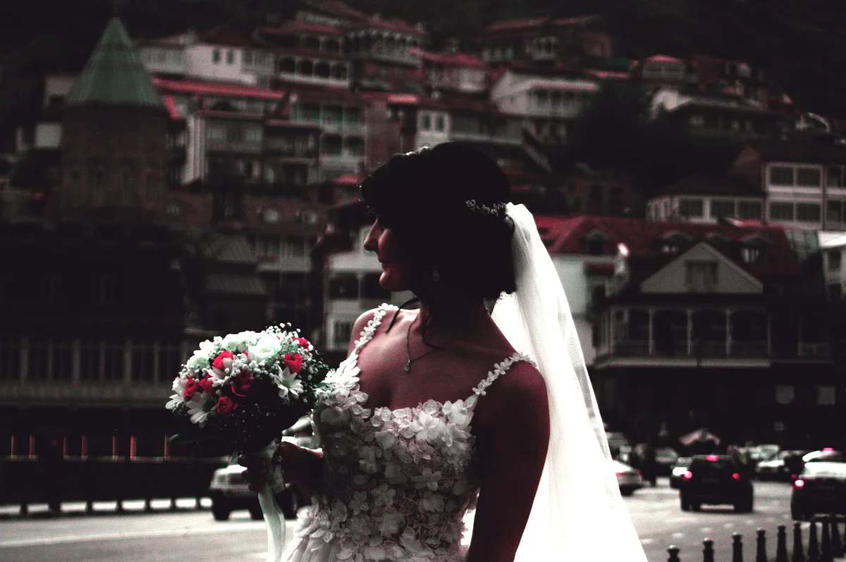 Bride in white gown holding bouquet with cityscape background, exuding elegance and grace.
