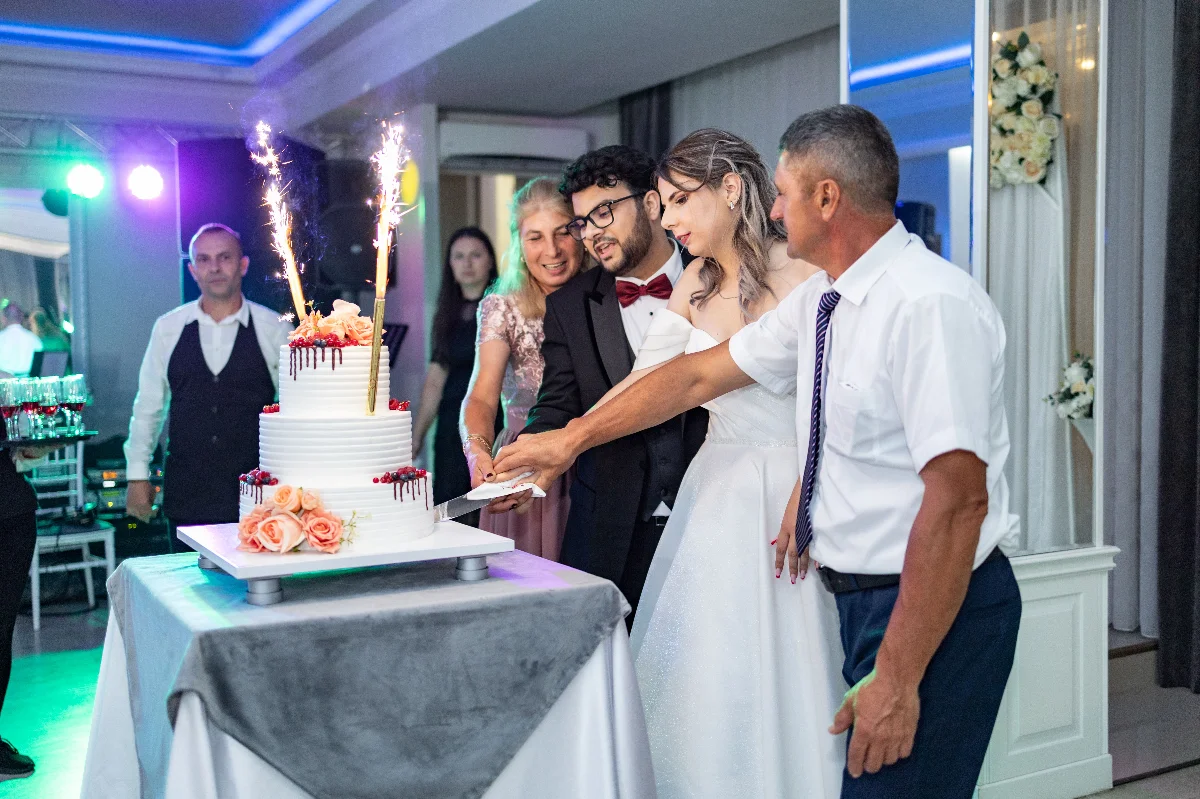 Couple cutting wedding cake with family during a lively reception.