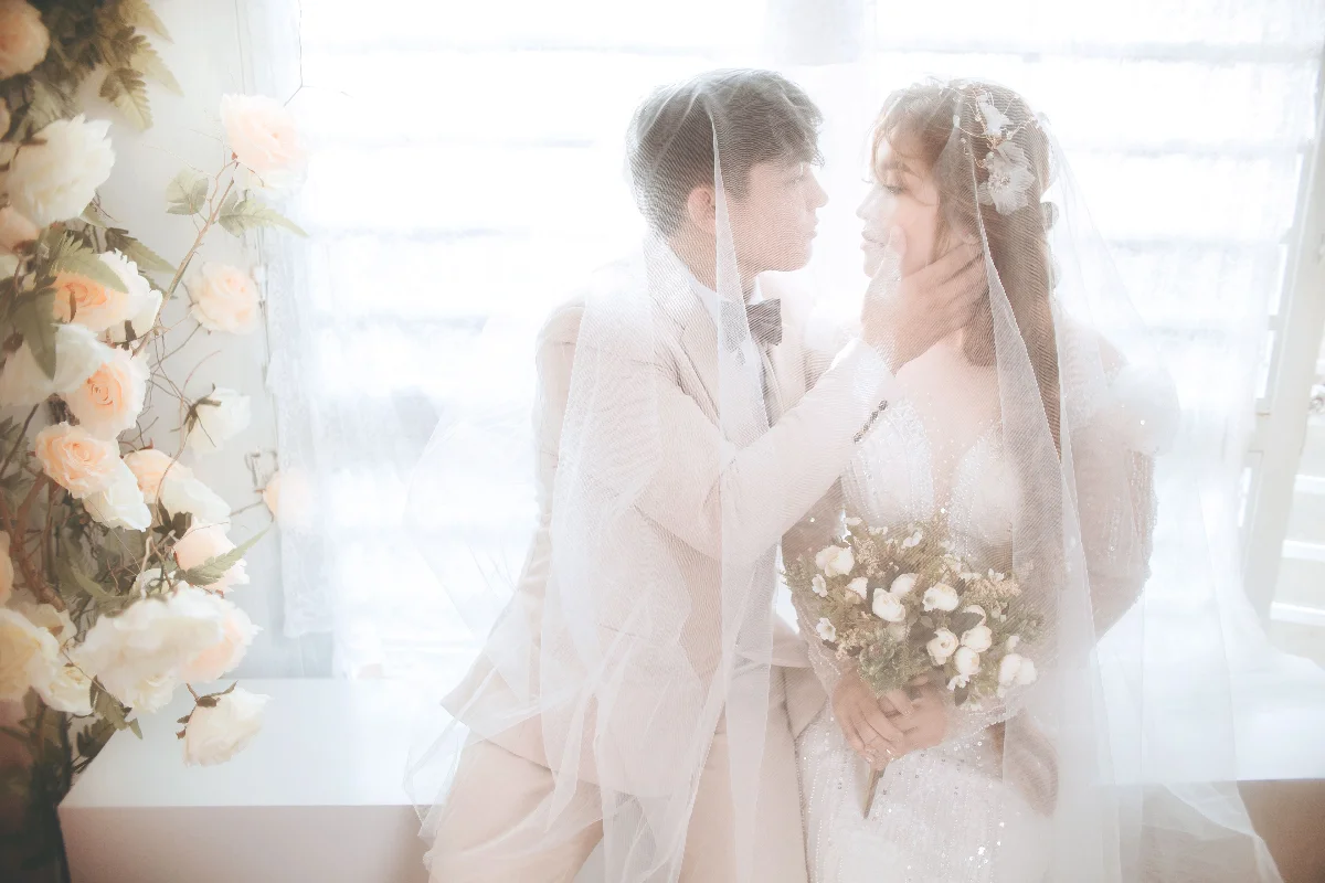 Romantic wedding photo of a couple in elegant attire under a veil, embracing love.