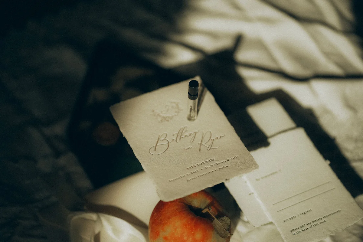 Artistic flat lay featuring an elegant save the date card with soft shadows, an apple, and a perfume vial.