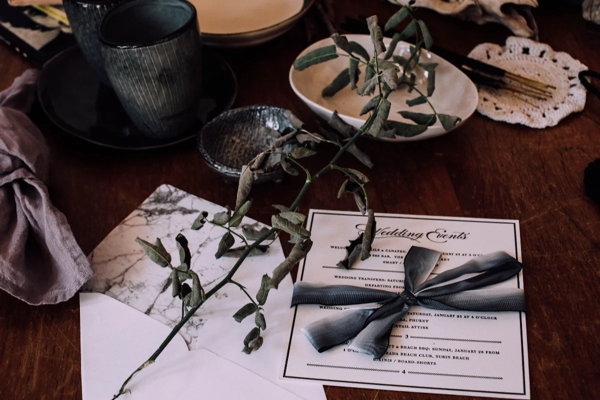 High angle of wedding invitation on wooden table among ceramic utensil near branch of dry plant and decorations