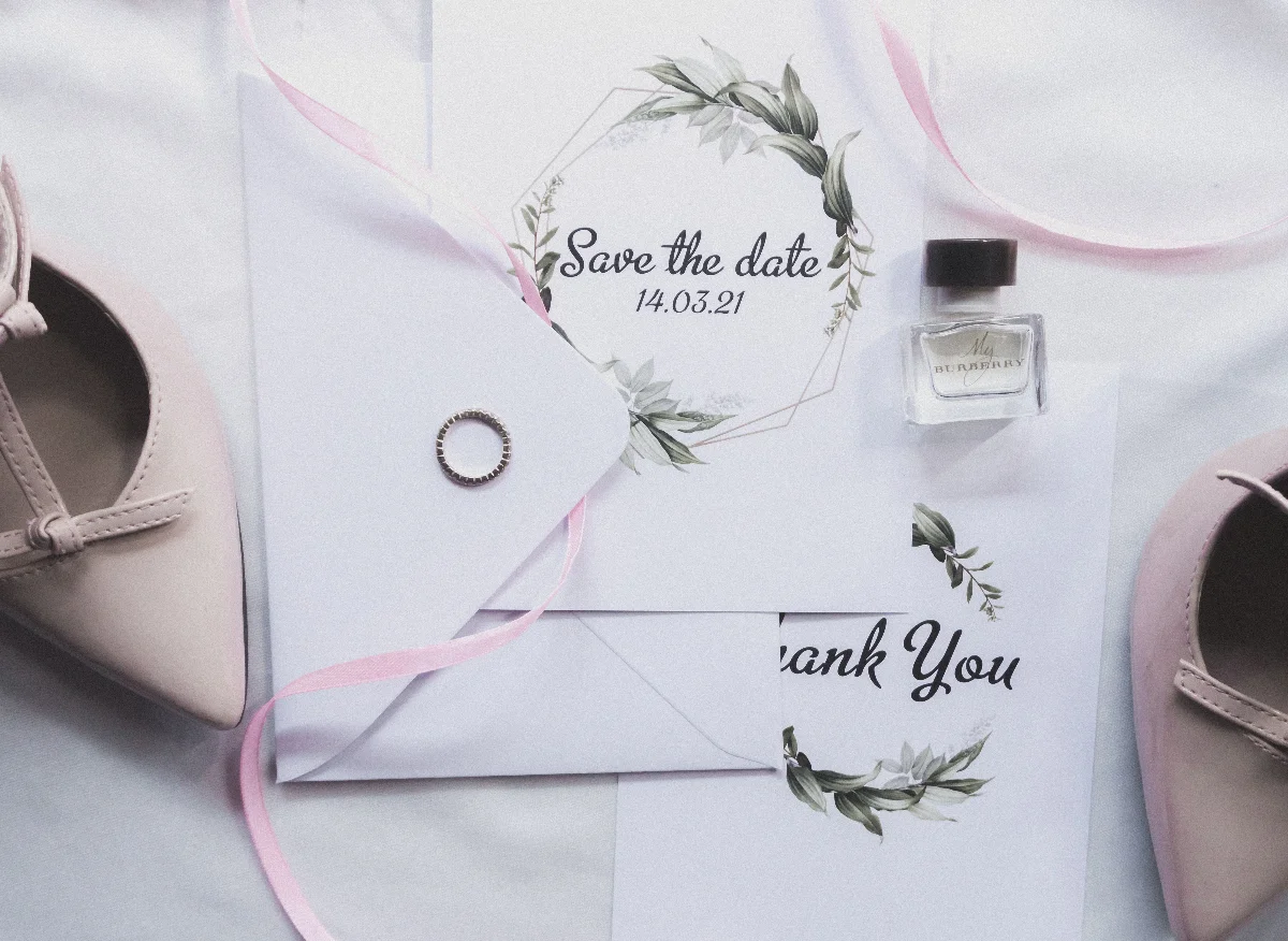 Stylish flat lay of wedding invitations, ring, perfume, and shoes for a chic celebration.