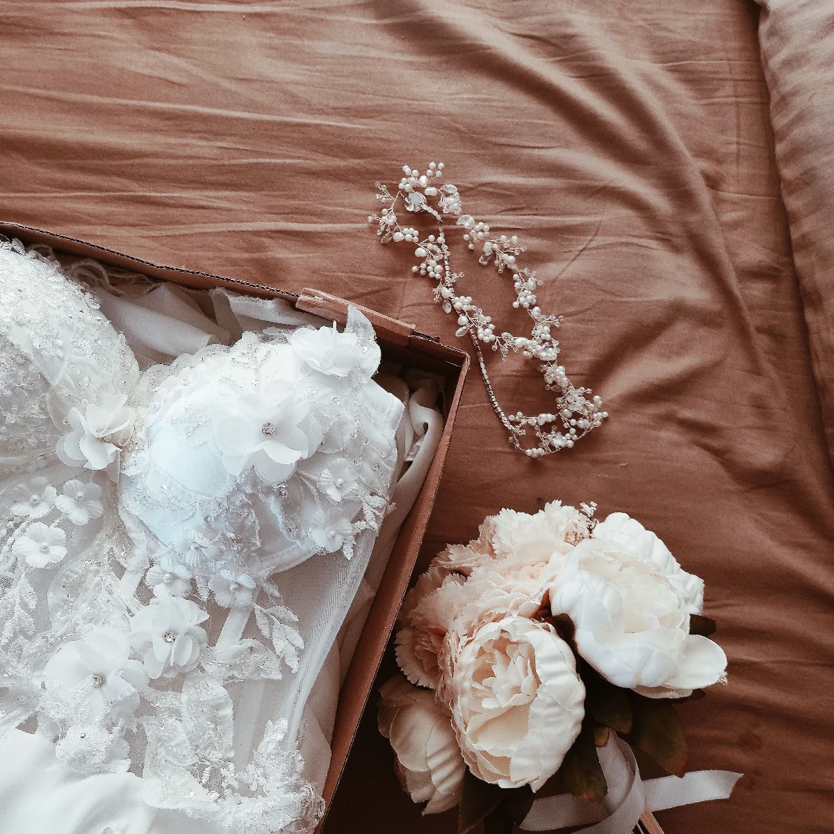 A beautiful wedding dress with a floral bouquet and accessories on a bed.