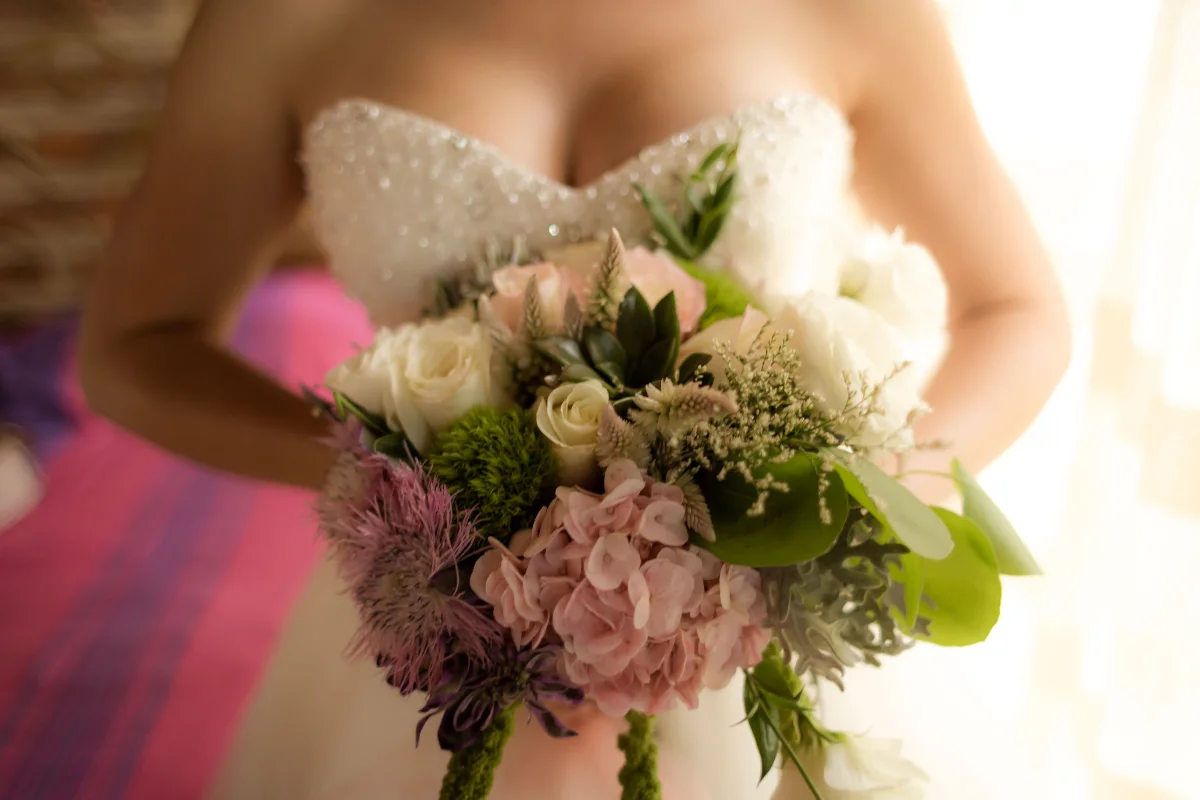Close-up of a bride holding a white and pink flower bouquet, symbolizing wedding elegance.