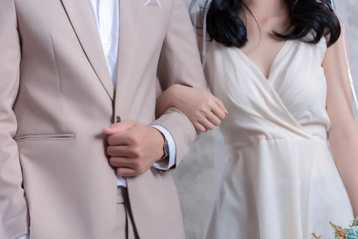 Close-up of a bride and groom in elegant attire holding arms, capturing love and unity.