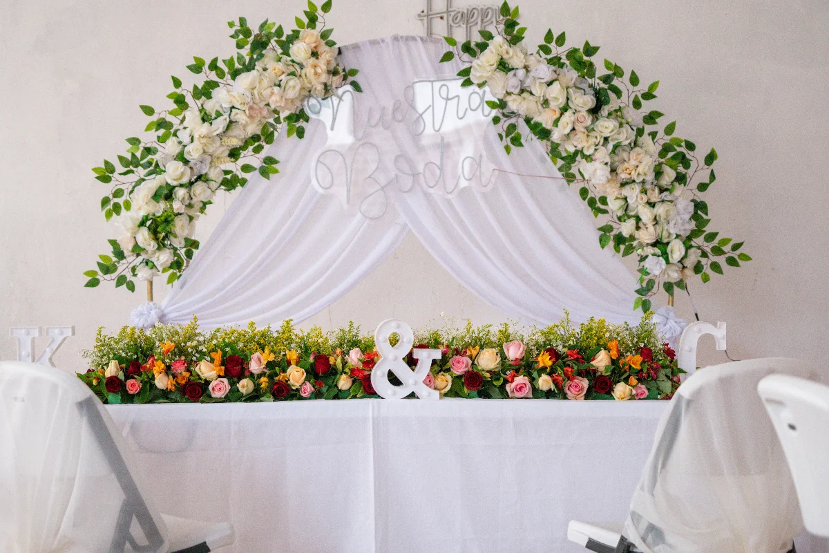 Beautifully decorated wedding table adorned with roses, greenery, and draped white fabric.