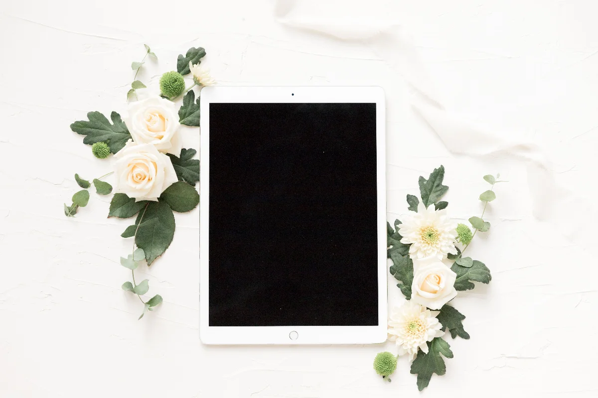 Stylish flatlay with white roses, chrysanthemums, and a digital tablet on a light background.