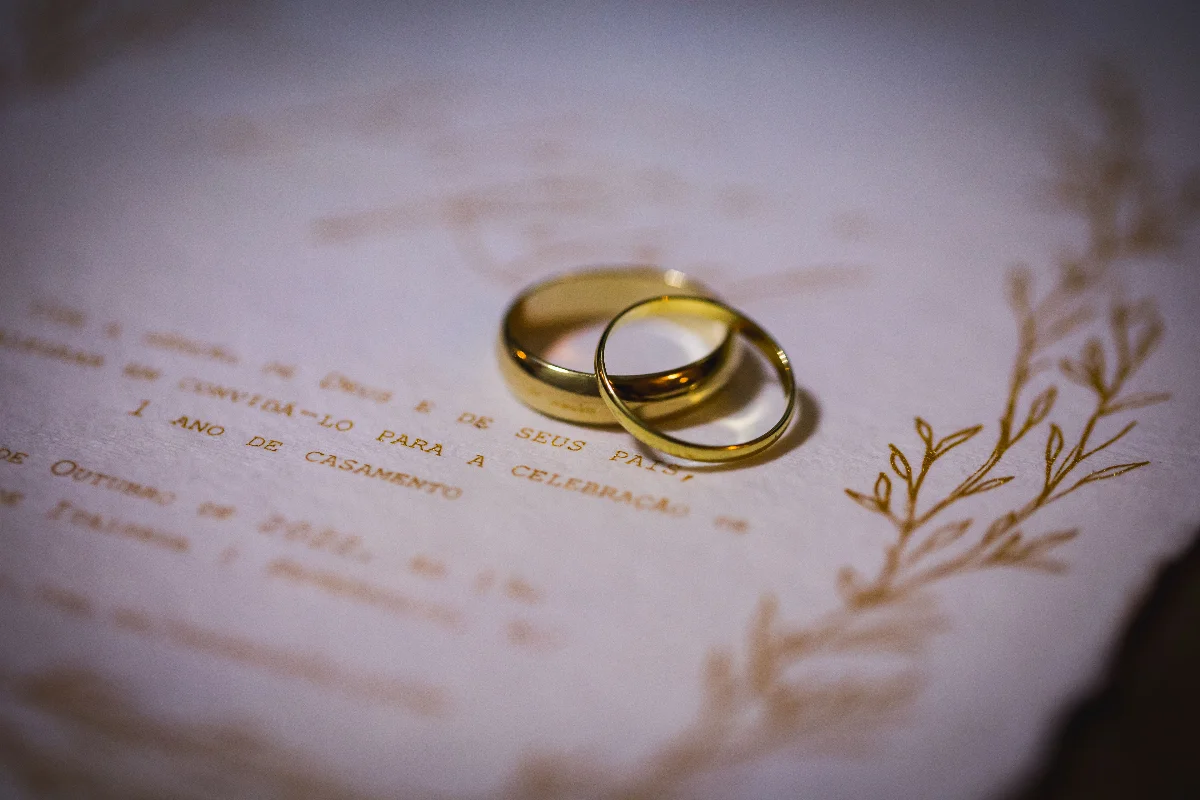 Close-up of gold wedding rings on a white wedding invitation with elegant floral design.