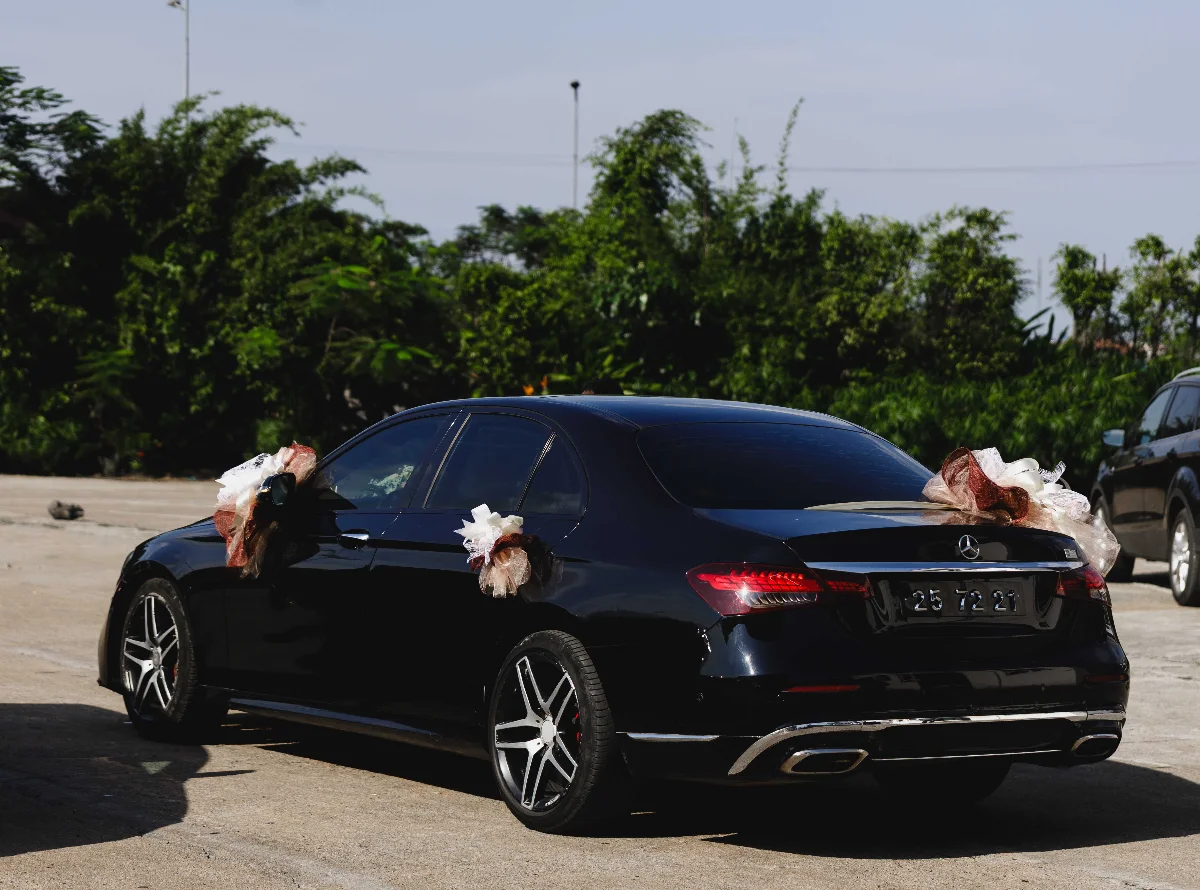 A stylish black car decorated with bows for a wedding, parked outdoors.