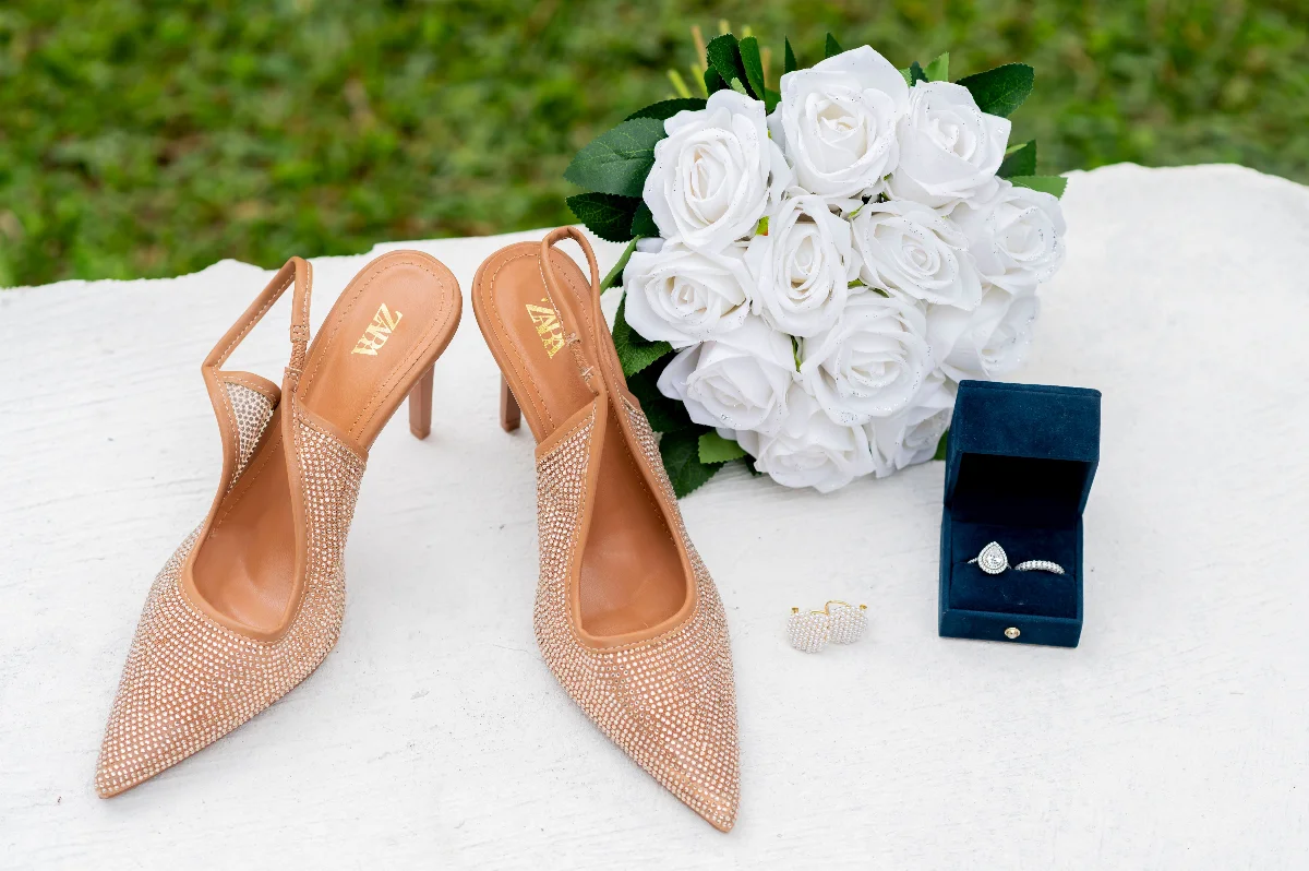 Elegant display of wedding shoes, white roses, and jewelry on a table.