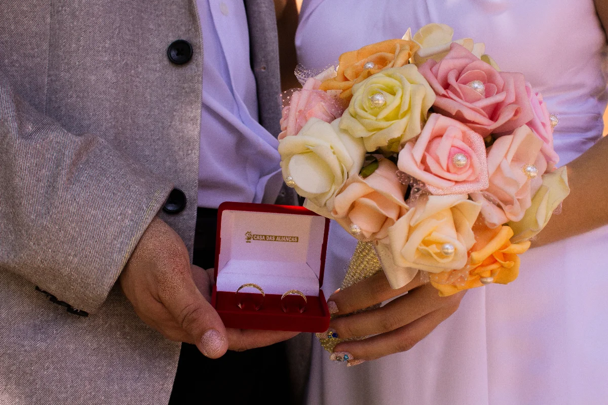 Close-up of couple holding wedding rings and colorful flower bouquet, symbolizing love.