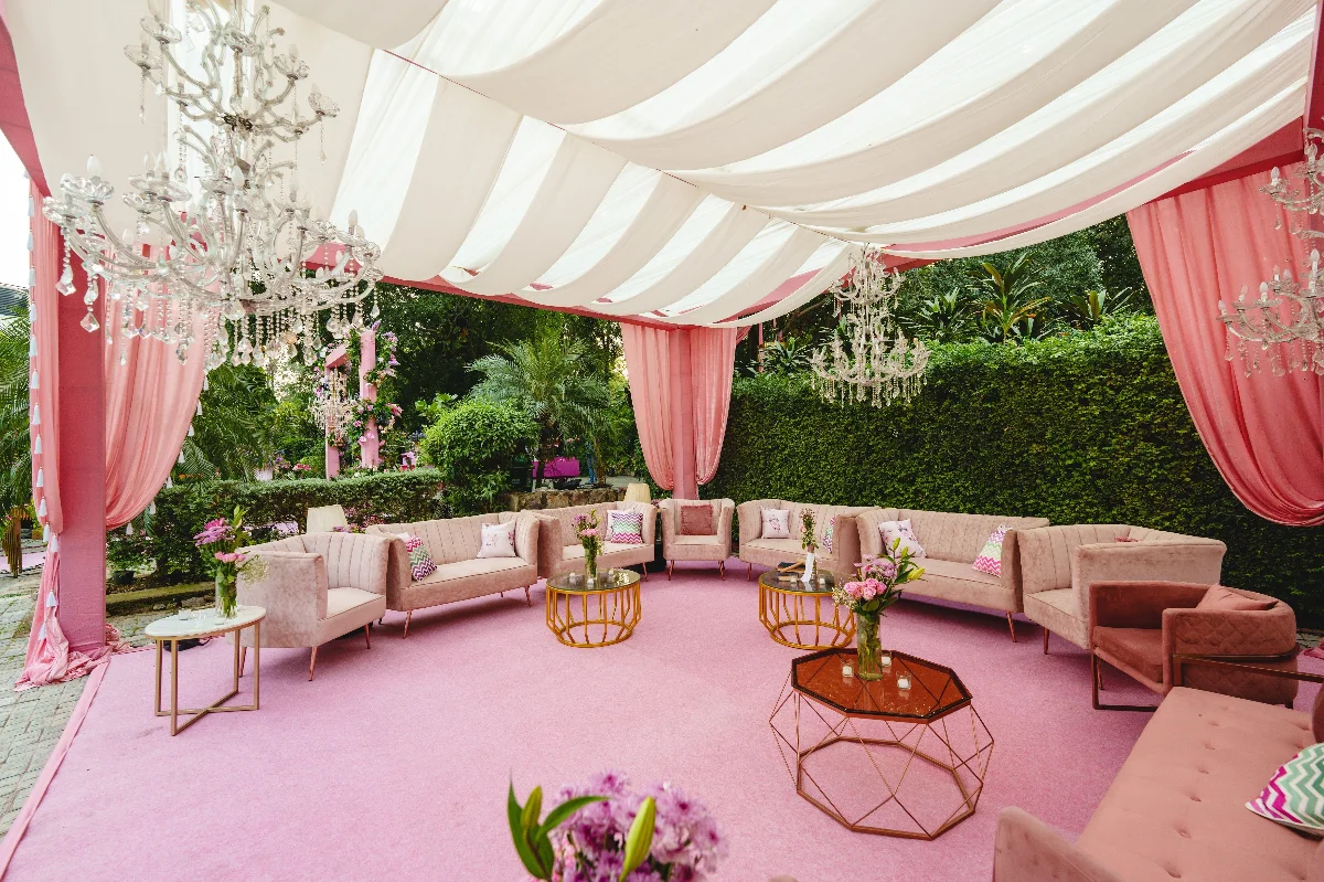 Luxurious outdoor lounge setup with pink drapery and chandeliers, perfect for weddings or events.