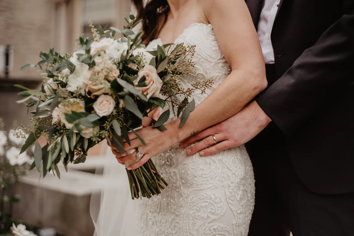 Lovely wedding scene showing a bride holding a bouquet and groom embracing, symbolizing love and togetherness.
